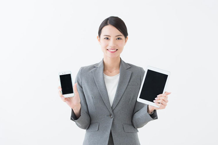 iPhoneとiPadを手に持ったスーツの女性
